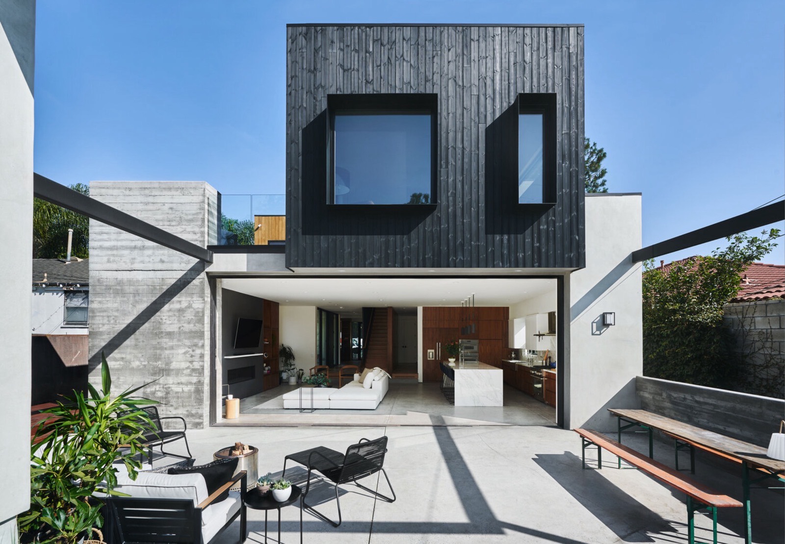 Completed Farnsworth Builders custom home — dark timber-clad upper volume over an open living space and concrete terrace.
