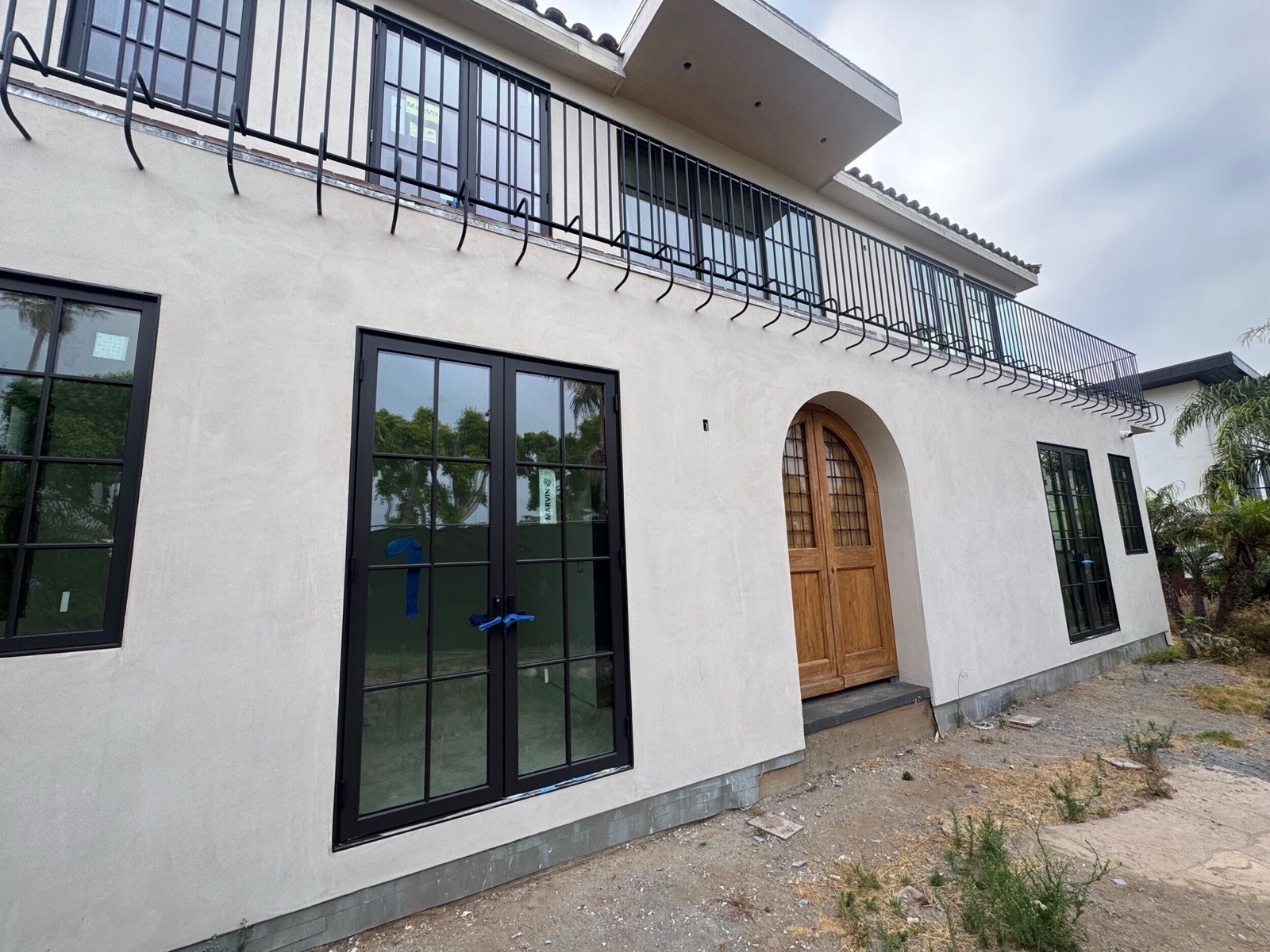 Farnsworth custom home under construction — stucco exterior with black steel windows and an arched timber entry, before final grading.
